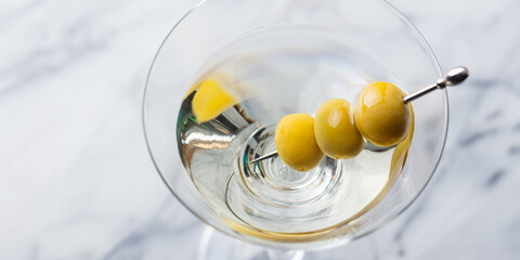 Martini cocktail with green olives. Marble background. Close up.