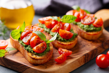 Pesto bruschetta, crostini with tomato, fresh basil on wooden cutting, serving board. Grey background. Close up.
