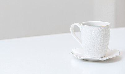 white porcelain cup on a table indoors. White saucer and cup of coffee on white table. side view