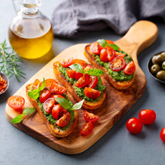 Tomato, pesto bruschetta, crostini with fresh basil on wooden serving board. Grey background. Close up.