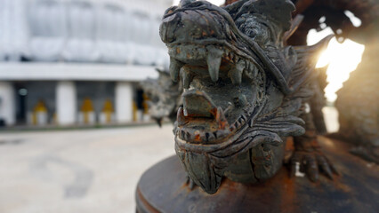 Three ancient dragons in the rays of the sun on the bell. Gradually covered with rust. Made of metal. The bell is next to the Big Buddha. Beautiful statues. Secured with a metal chain. Phuket Thailand