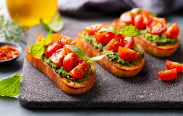 Tomato, pesto bruschetta, crostini with fresh basil on serving board. Close up.