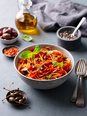 Pasta, spaghetti with tomato sauce, olives and fresh basil. Grey background.