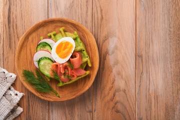 Savory waffles. Breakfast green waffles wild garlic or spinach with egg, tomato, salmon on wooden plate for breakfast on old wooden background. Light dinner, lunch or breakfast. Top view. Mock up.