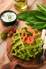 Green Belgian waffles. Spinach or wild garlic or pesto waffles with red salmon and cream sauce on black plate over dark rustic wooden background. Delicious breakfast, snack, brunch. Mock up