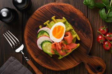 Savory waffles. Breakfast green waffles wild garlic or spinach with egg, tomato, salmon on wooden plate for breakfast on old dark wooden background. Light dinner, lunch or breakfast. Top view. Mock up