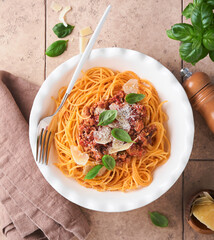 Pasta spaghetti Bolognese. Tasty appetizing italian spaghetti with bolognese sauce, tomato sauce, cheese parmesan and basil on white plate on old beige tiles table background. Top view.
