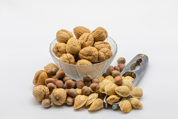 Walnuts, hazelnuts and almonds in a glass bowl with a nutcracker, isolated on a white background