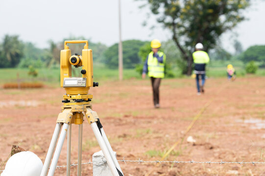 A team of survey engineers working with a theodolite at a commercial building construction site.