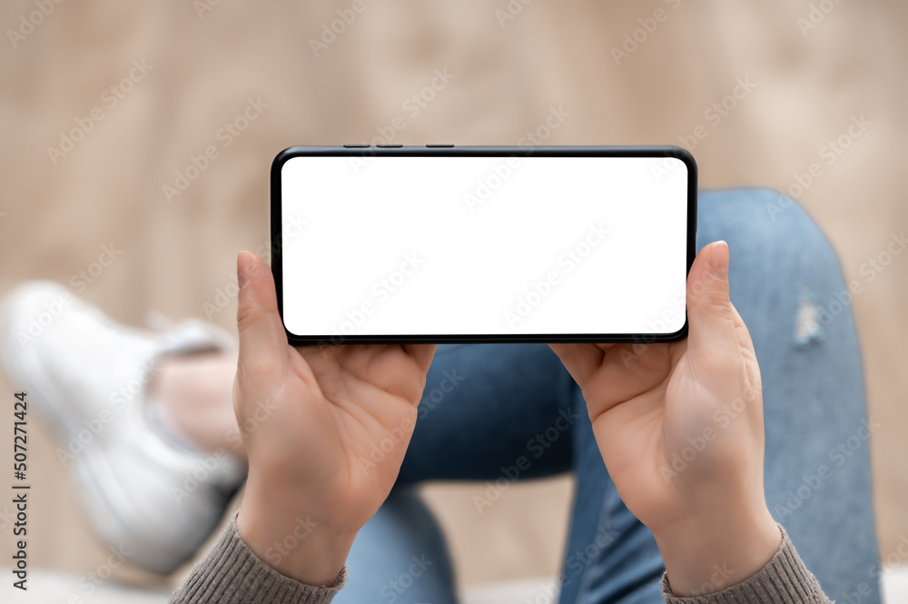Poster top view mockup image of woman holding mobile phone horizontally with blank white screen. woman usin