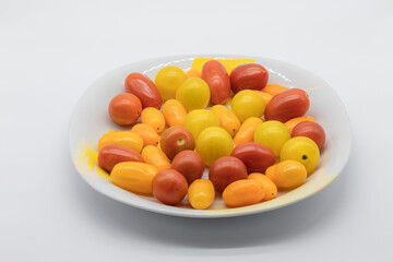 Different types of tomatoes in size and color, pear tomato, cherry tomato, in a round plate on a white background.