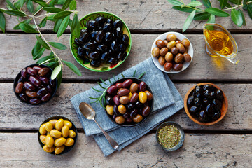 Assorted olives on a plate with olive tree brunches. Wooden background. Top view.