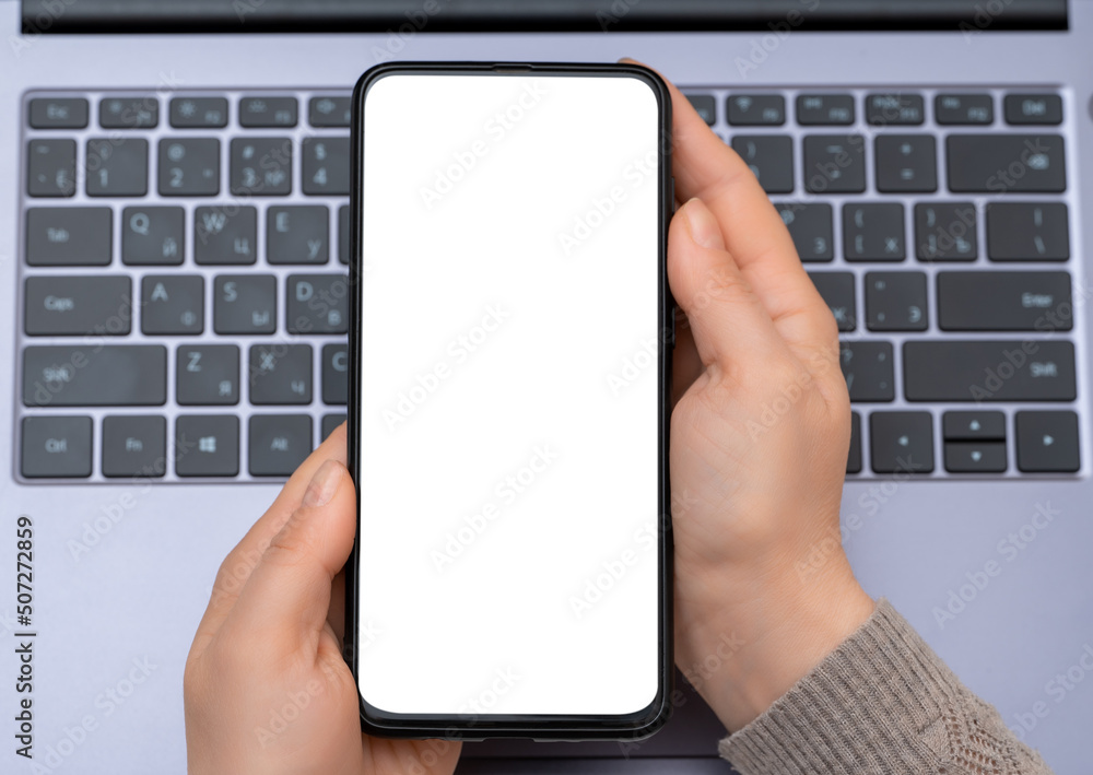Poster mockup cellphone. top view mockup image of hands holding blank white screen mobile phone with laptop