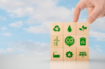 Climate neutral long term strategy. Hand put wooden cubes with green icon and green icon on blue background. Climate neutral long term strategy. Wooden cube with carbon neutral, green factory icon.