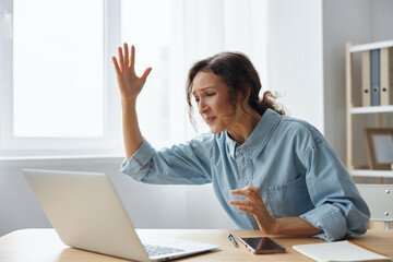 Furious angry evil beautiful curly businesswoman hates computer crash having problem with broken laptop swings at gadget raises hands up sitting at home office. Freelancer work concept. Copy space