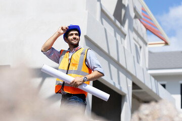 A smiling caucasian builder in a white hard hat and yellow fluorescent jacket holds clipboard, stands on the roof, inspects construction site and makes notes. - Powered by Adobe
