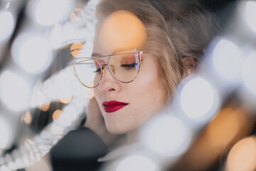 Fototapeta Nowoczesny portret dziewczyny w okularach wśród lampek bokeh obraz