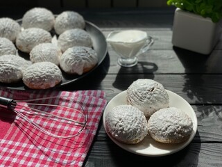Homemade cookies with white icing on a black table. White dessert on a white plate. Whisk on a red kitchen towel.
