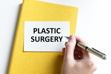 Plastic Surgery inscription on a white card on a white background, a person's hand writes text with a pen