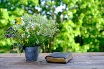 book in black cover, bouquet of wild flowers, family bible lie on wooden table in garden, blurred...
