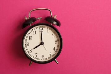 black vintage style alarm clock isolated on a pink background