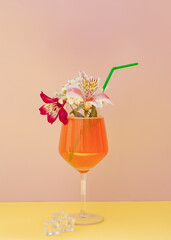 Fresh homemade drink with flowers and ice on pink and yellow background.