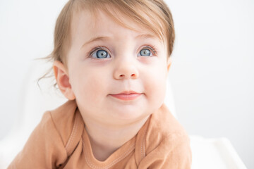 portrait of cute baby girl 10 months with blue eyes in brown bodysuit on white background - obrazy, fototapety, plakaty