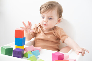 cute baby girl playing with colorful wooden blocks at child chair. early children development
