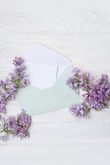 paper envelope with empty card and spring lilac flowers on white wooden background. spring season. women's day, mother's day, Valentine's day greeting concept. mock up. copy space