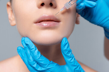 Cropped image of young girl doing cosmetology injections on lips isolated over grey studio...