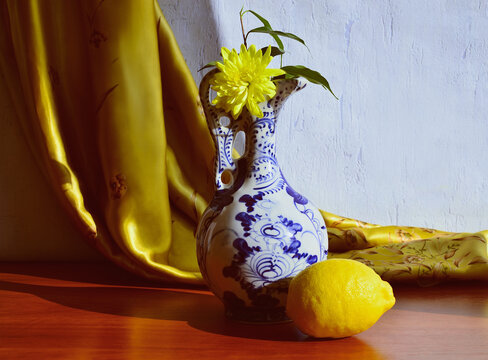 Vintage still life with a porcelain jug and lemon and a background of silk gold fabric.