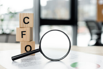 magnifying glass near cubes with cfo letters and document on desk.