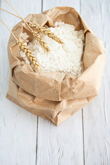 Wheat flour in paper pack with ears of wheats on white wooden table.