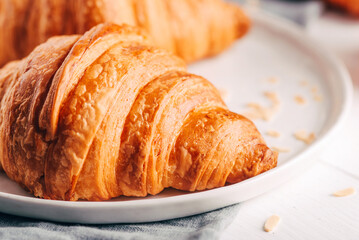 Plate with fresh croissants on white wooden table. Close up.