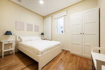 Bedroom with white wooden double bed, matching two-door wardrobe, windows with blinds and oak parquet flooring and white duvet cover