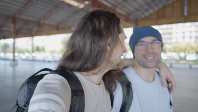 Two happy young men walk, talk and laugh with camera in selfie mode