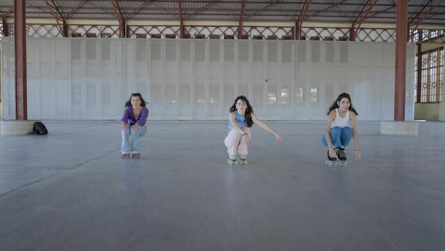 Three young women roller skate toward camera while holding one foot