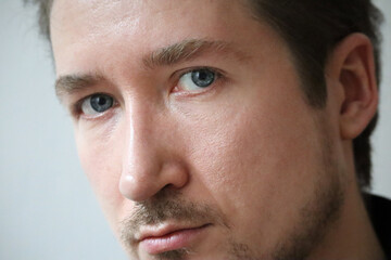 Close-up of the face of a young man with blue eyes, natural skin and a small beard