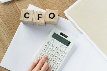 top view of chief financial officer using calculator near cubes with cfo lettering.