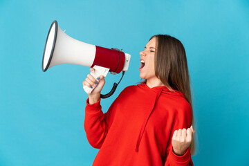 Young Lithuanian woman isolated on blue background shouting through a megaphone to announce something in lateral position