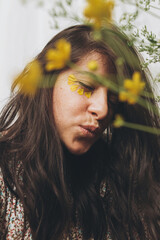 Beautiful happy woman with yellow petals on face posing with wildflowers in sunny room. Portrait of...