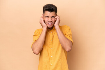 Young caucasian man isolated on beige background frustrated and covering ears