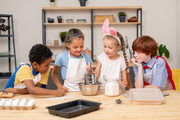 Children wearing apron browsing Internet on digital tablet in order to find recipe of appetizing cookie