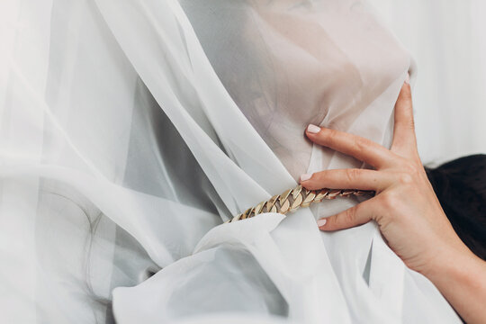 Portrait of young female covered with light fabric and hand on neck. Self care concept. Social isolation and pressure. Sensual woman under veil posing with golden necklace in room. Suffocate
