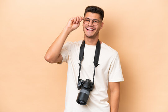 Young photographer caucasian man isolated on beige background with glasses and happy