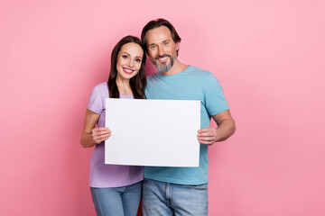 Portrait of two cheerful positive people hold demonstrate empty space list isolated on pink color background