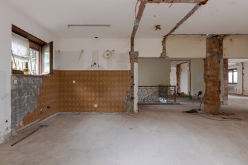 Large bright room with many windows of an old villa undergoing demolition and renovation. The walls have been knocked down and the floor is gone.