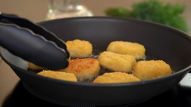Kitchen tongs flip fried chicken nuggets in sizzling oil in hot frying pan. Nuggets fry with crispy crust.