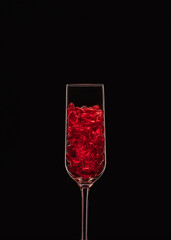 Champagne flute filled with transparent red heart shape crystals backlit and isolated on black background. Love and celebration concept. Copy space.