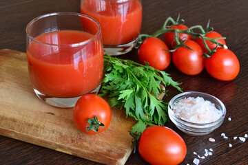 tomato juice in drinking glasses with garden tomatoes and greens on cutting board, close-up